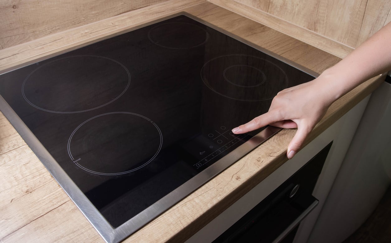 A woman's finger presses the inclusion of a modern induction hob in the kitchen. Electric induction cooker. Copy space for text